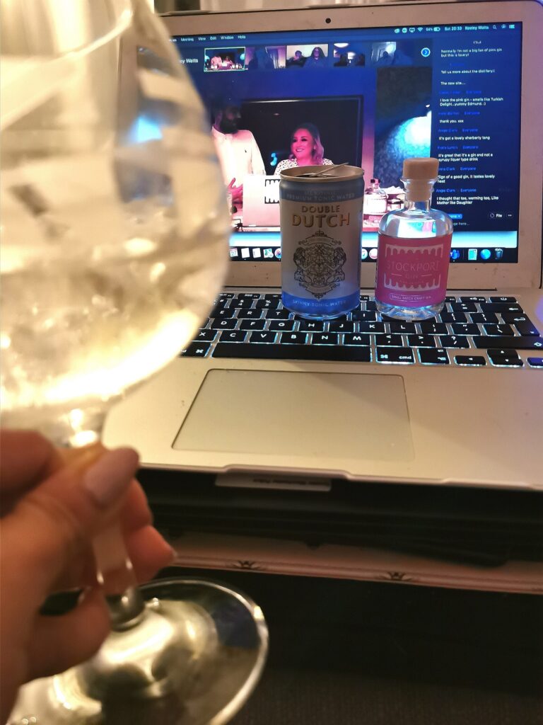 a glass filled with gin and tonic lifted to cheers with a laptop in the background streaming the stockport gin live virtual tasting